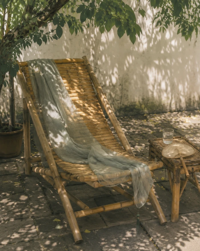 Ein Bambusliegestuhl im Schatten eines Sommernachmittags mit Fächer und Wasser