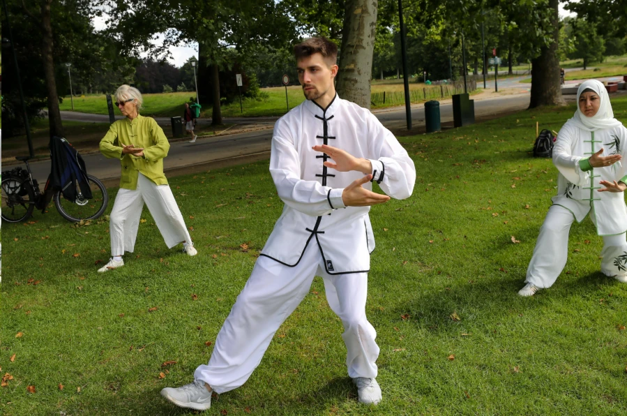 Une personne debout calmement en posture qigong sous un vieil arbre dans un parc brumeux