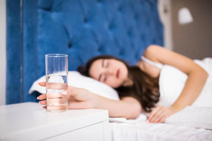 A person sitting up in bed before dawn, hand on the edge of the bed, moonlit window